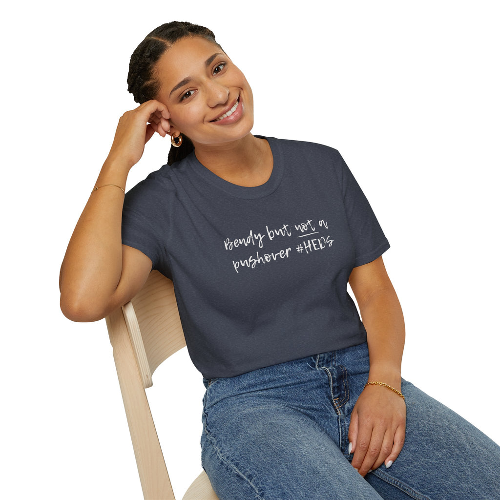 Woman wearing a dark gray t-shirt with 'bendy but not a pushover' text, sitting on a chair.