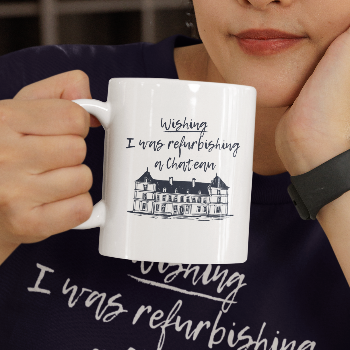 Person holding a mug with text and a chateau illustration, with the words, 'wishing i was refurbishing a chateau' wearing a matching shirt.