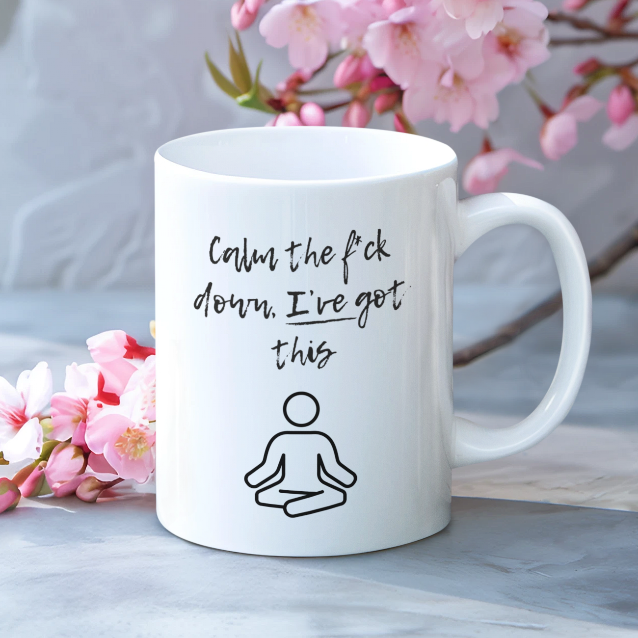 White mug with text 'calm the f*ck down I've got this' and a drawing on a surface with cherry blossom branches in the background. Prefect burnout gift from pretty bold prints