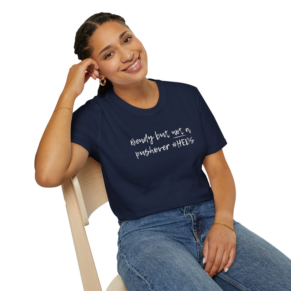 Woman wearing a navy blue t-shirt with 'bendy but not a pushover' printed on it, sitting on a chair.